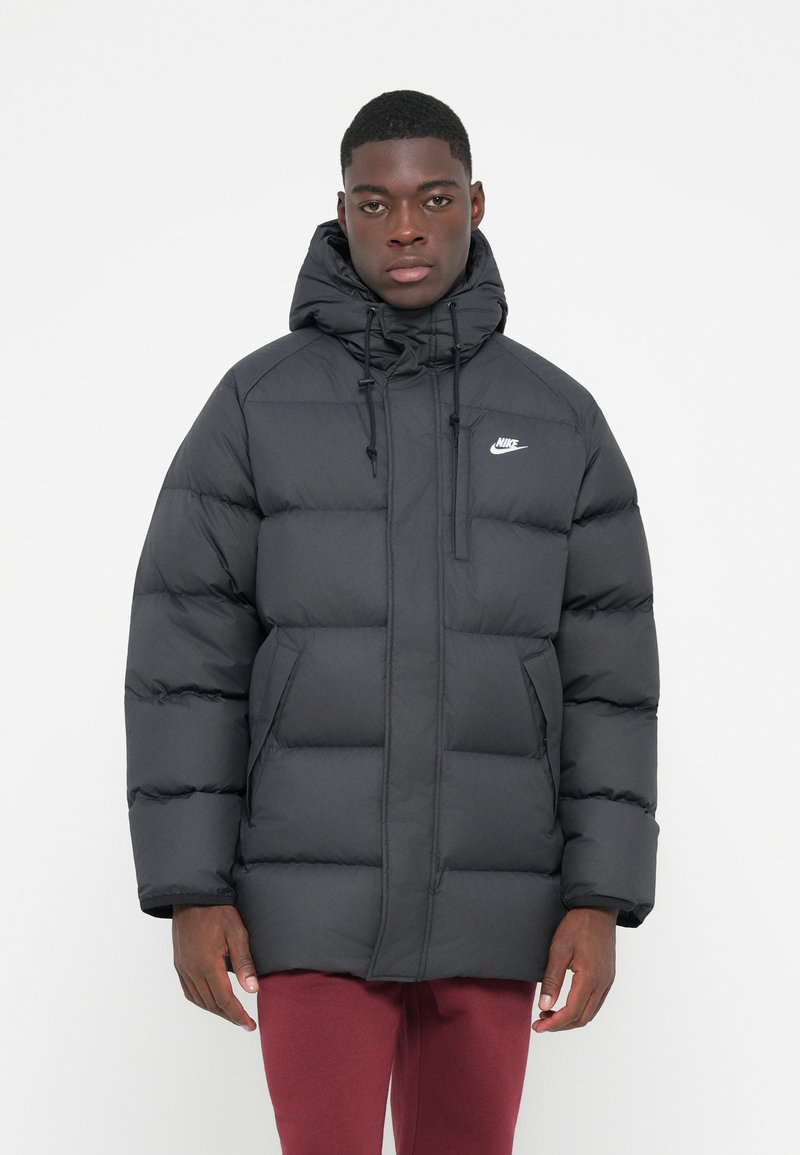 Svart dunjakke med hette, quiltet design, frontlås, sidelommer og en liten hvit Nike-logo på brystet.