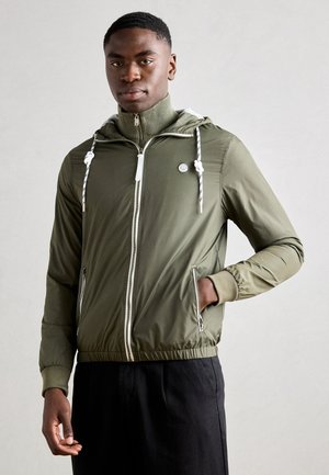 Olivegrüne leichte Jacke mit Kordelzugkapuze, frontalem Reißverschluss, Seitentaschen und gerippten Akzenten. Texturierten Stoff mit elastischen Bündchen.
