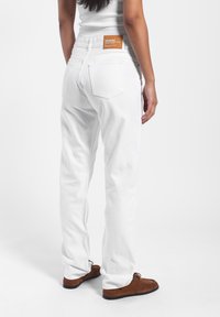 Vaqueros de denim blanco con corte recto, que cuentan con dos bolsillos traseros y una etiqueta marrón en la cinturilla. Textura suave, diseño minimalista.