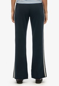 Navy wide-leg pants with side slits and cream stripes, featuring a soft texture, elastic waistband, and a relaxed fit.