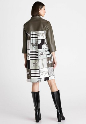 Vrouw draagt een knielange jurk met een olijfgroene leren top en een patchwork rok met paard- en streeppatronen, gecombineerd met zwarte kniehoge laarzen.