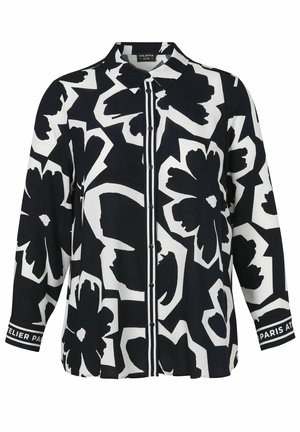 Chemise boutonnée noire et blanche avec de grands motifs floraux abstraits et des poignets rayés comportant du texte.