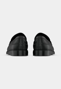 Mocassins en cuir noir à finition lisse, bout arrondi et petit talon carré, avec des détails de couture discrets sur les côtés.
