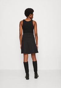 Un haut sans manches noir associé à une jupe évasée noire. La tenue a une taille cintrée et le mannequin porte des bottes noires hautes jusqu'au genou.