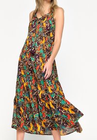 Bezramenné šaty midi s volným střihem a vícebarevným tropickým a zvířecím potiskem, s vázacím výstřihem a vícevrstvou sukní, na stojící ženě.