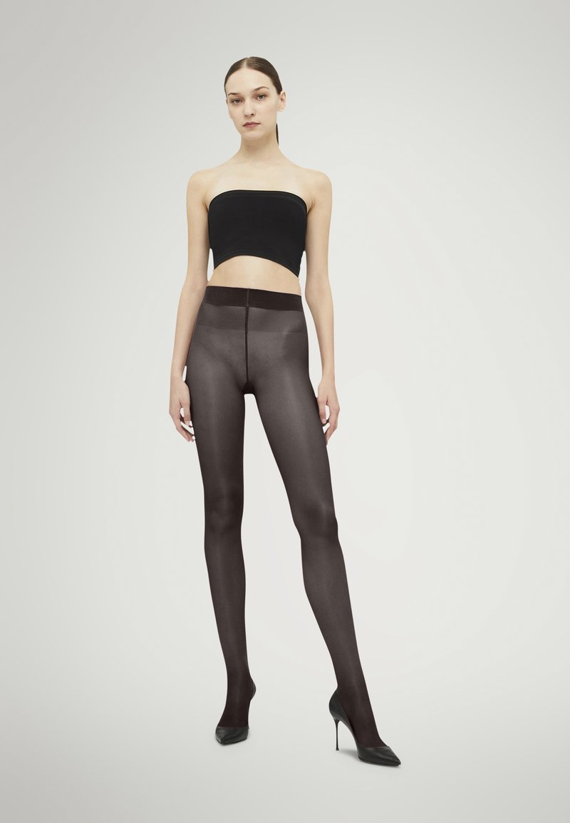 Leggings neri trasparenti con una cintura ampia, texture liscia e un design aderente, indossati con tacchi a spillo e un top corto nero.