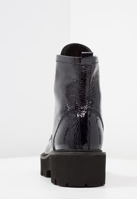 Botte de cheville en cuir verni noir avec un fini texturé, semelle en caoutchouc noir robuste et une languette en boucle à l'arrière pour un enfilage facile.