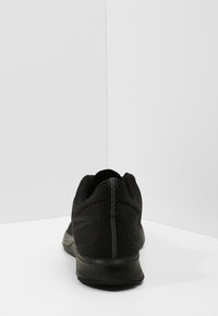 Chaussure de sport noire avec un dessus en mesh et des accents texturés. Dotée d'un col rembourré et d'une semelle en caoutchouc lisse. Design minimaliste.