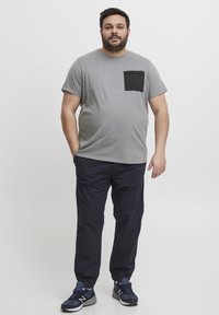 Grijs t-shirt met korte mouwen en een zwarte borstzak, gecombineerd met navy broek en navy sportschoenen. Eenvoudig ontwerp en een comfortabele pasvorm.