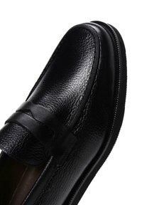 Black leather loafer shoe with a textured surface, decorative strap, and smooth edges. Features a rubber sole for grip and comfort.