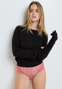 Maglione nero a maniche lunghe con scollo ampio; abbinato a mutandine rosa a fantasia con orli seghettati. Tessuto morbido, vestibilità comoda.