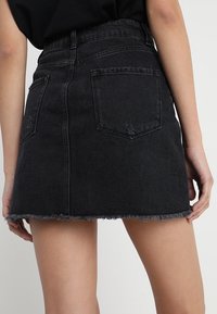 Mini gonna in denim nera con orlo sfilacciato, vita alta e due tasche posteriori. Il materiale sembra robusto con una superficie liscia.