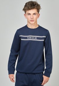 Sudadera de manga larga azul marino con puños acanalados, que presenta rayas horizontales grises en contraste y bordado del logo en el pecho. Tejido suave.