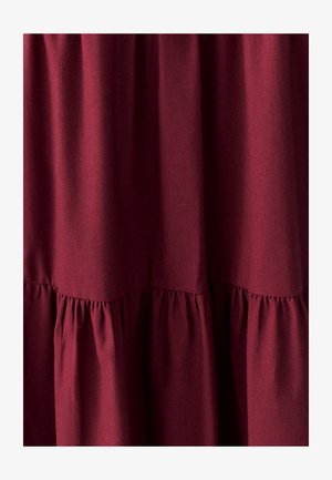 Burgundin kangas sileällä tekstuurilla, jossa on poimutetuja yksityiskohtia helman kohdalla, luoden virtaavan, kerroksellisen muotoilun.