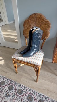 Bottes de cowboy noires brillantes posées sur une chaise rayée. Les bottes présentent des bouts pointus et des motifs de couture complexes le long de la tige.
