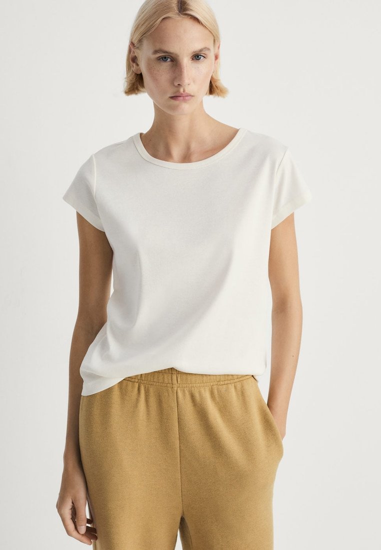 Vit t-shirt med kort ärm i mjukt tyg och rund halsringning, tillsammans med ljusbruna joggingsbyxor med elastisk midja. Minimalistisk design.