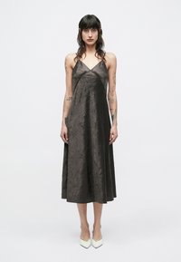 Tumši brūnas krāsas bezroku kleita ar saburzītu tekstūru, V veida kakla izgriezumu un A līnijas siluetu. Valkāta ar gaiši krāsainām smailām augstpapēžu kurpēm.