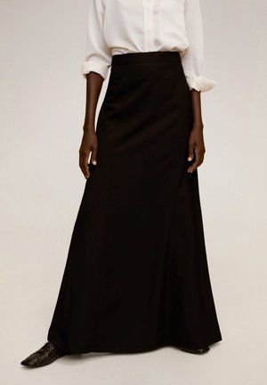 Falda maxi negra de tela suave. Diseño de cintura alta con una silueta acampanada. Combinada con una camisa blanca de cuello y zapatos de punta.