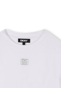 Camiseta blanca de algodón con cuello redondo, que presenta un pequeño logo de DKNY bordado en plata en la parte delantera y un diseño liso.