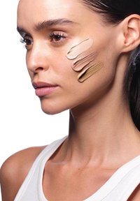 Quattro campioni di fondotinta in diverse tonalità della pelle applicati sulla guancia di un modello, che mostrano texture cremose e gradienti di colore sulla pelle chiara.