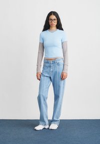 Ανοιχτό μπλε εφαρμοστό t-shirt το οποίο είναι επενδεδυμένο με ένα γκρι μακρυμάνικο τοπ. Ψηλόμεσα ανοιχτό μπλε ριγωτά τζιν. Λευκά παπούτσια, μεγάλα γυαλιά.