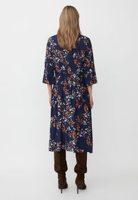 Marinblå blommig klänning med trekvartsärm, prydd med röda, orange och vita blommönster. Tyget har en mjuk och flödande textur och en markerad midja.