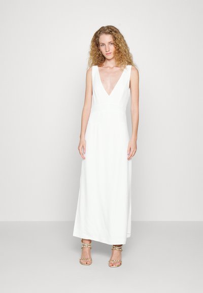 Vestido maxi branco, sem mangas, com um decote V profundo, corpete justo e saia fluída. Com sandálias com detalhes em dourado. Textura suave.