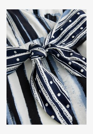 Sinivalkoinen kuvioitu kangas, jossa on pystysuorat raidat ja rusettiyksityiskohta. Materiaalissa on pehmeä rakenne ja pistekuvioita.