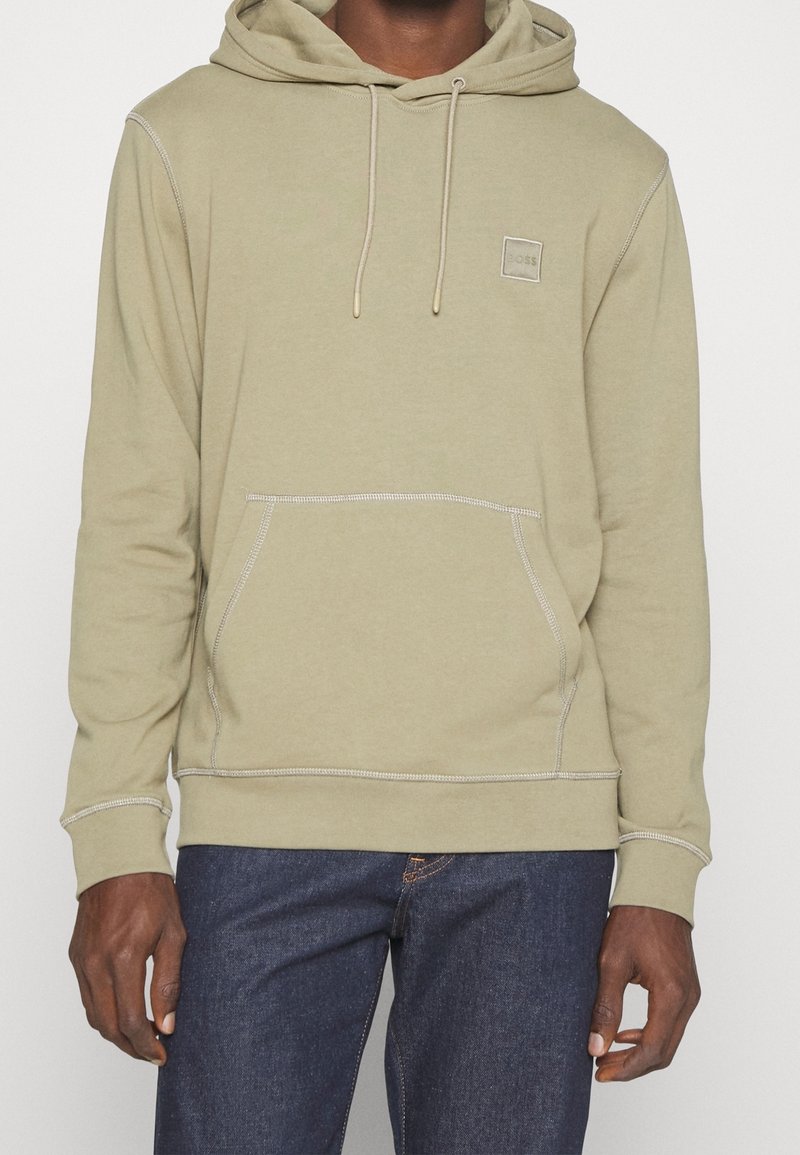 Oliven grøn hoodie med en frontlomme, snoretræk i hætten og kontrasterende syninger. Har et lille mærke på brystet.