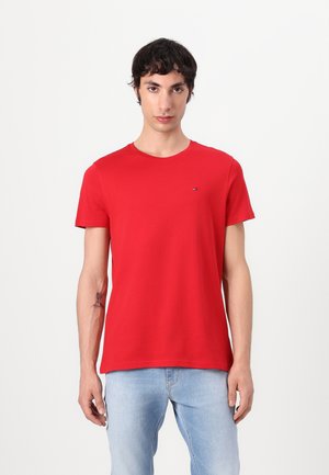Rotes T-Shirt mit kurzen Ärmeln aus Baumwolle, mit Rundhalsausschnitt und einem kleinen Logoschmuck auf der Brust; kombiniert mit hellblauen Jeans.