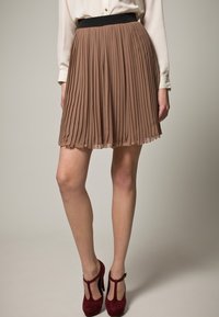 Falda marrón plisada con una cinturilla negra, que presenta un diseño fluido y una textura ligera, combinada con zapatos de tacón burdeos.