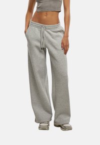 Pantaloni della tuta larghi grigio chiaro con vita elastica e cordino. Realizzati in tessuto morbido, presentano tasche laterali e una vestibilità rilassata.
