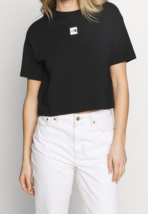 Black cropped t-shirt made of cotton, featuring a small white logo patch on the chest. Paired with high-waisted white jeans.