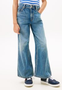 Φαρδιά τζιν παντελόνια από ανοιχτό γαλάζιο denim με ψηλή μέση, διακοσμημένα με τσέπες μπροστά και διακριτικό ξεθώριασμα. Φορεμένα με ναυτικομπλε αθλητικά παπούτσια και άσπρα κορδόνια.