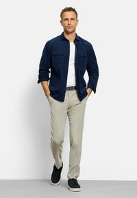 Marineblaues Hemd mit Knöpfen, weißes Unterhemd, beige Hose und schwarze Turnschuhe; das Hemd hat zwei vordere Taschen und eine entspannte Passform.