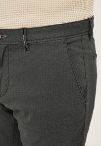 Close-up of dark gray textured pants with front pocket and belt loop, complemented by a beige waffle-knit top tucked in.