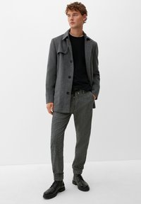 Grå uld-blandingsfrakke med knaplukning, sort crew-neck sweater, strukturerede grå joggerbukser og sorte snørebåndsstøvler.