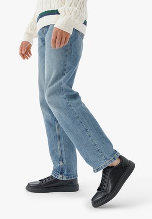 Jeans in denim azzurro chiaro con vestibilità a gamba dritta, abbinati a sneaker nere. I jeans presentano cuciture visibili e sono leggermente consumati all'orlo.
