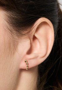 Złote kolczyki o zakrzywionym kształcie z kulistymi koralikami w różnych rozmiarach, delikatnie umieszczone w płatku ucha, odbijające światło.