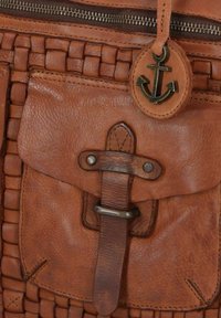 Borsa a mano in pelle marrone con un design intrecciato, tasca frontale con pattina, chiusura in metallo e decorazione a forma di ancora su un tirante della cerniera.