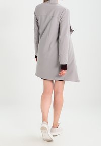 Jasnoszary płaszcz do kolan o lekko oversize'owym kroju, z kołnierzem i długimi rękawami, wykonany z gładkiego materiału z detalem w postaci guzika.