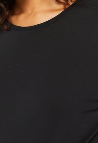 Černé tričko s kulatým výstřihem, vyrobené z hladkého materiálu; má jednoduchý, přiléhavý střih bez dalších vzorů nebo akcentů.