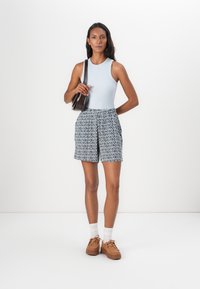 Light blue sleeveless top paired with patterned blue and white shorts. Brown handbag, brown lace-up shoes, and white ankle socks.
