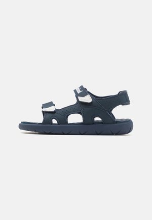Navyblå sandaler lavet af syntetisk materiale, med velcro-stropper, udskæringer til ventilation og en struktureret gummisål.