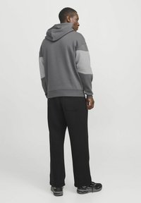Grau Hoodie mit strukturiertem Design, mit hellgrauen Akzenten an den Schultern. Kombiniert mit schwarzen weiten Hosen und schwarzen Sneakers.