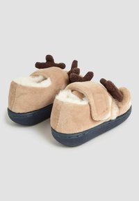 Pantofole in peluche beige con foderina morbida, suole blu e corna in tessuto marrone. Progettate con una cinghia in velcro per una facile vestibilità.