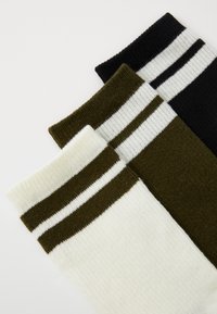 Three pairs of socks: white with two dark stripes, olive green with two light stripes, and black with two white stripes, all knitted.