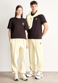 Μαύρα βαμβακερά T-shirts με κέντημα λογότυπου, κρεμ φόρμες με ελαστικές μανσέτες, φορεμένα με λευκά και μαύρα αθλητικά παπούτσια.