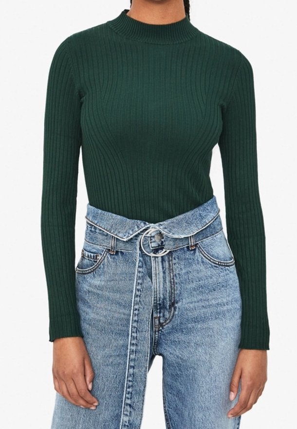 Grünes, geripptes Langarmoberteil mit hohem Kragen, kombiniert mit hochgeschnittenen, hellblauen Denim-Jeans mit tailliertem Design und fransigem Saum.