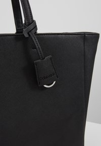 Sac cabas en cuir noir texturé avec deux poignées et une petite étiquette embossée Calvin Klein près du bord supérieur.